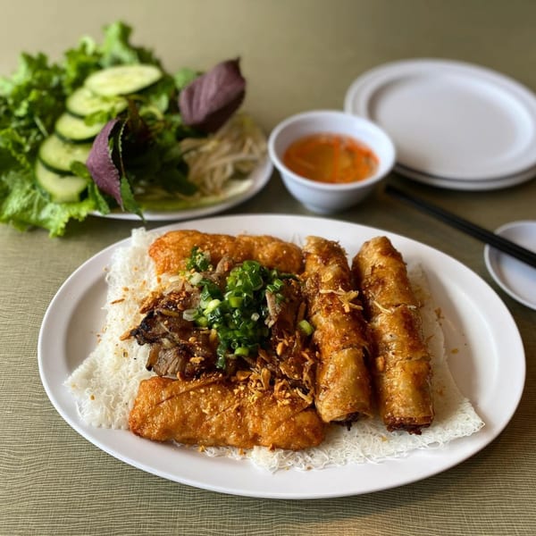 Golden Deli's Vietnamese grilled pork and crispy spring rolls over vermicelli, with fresh greens and dipping sauce.