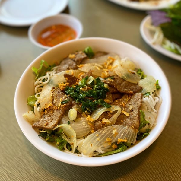A bowl of Vietnamese vermicelli noodles with beef, onions, lettuce, and fried garlic.