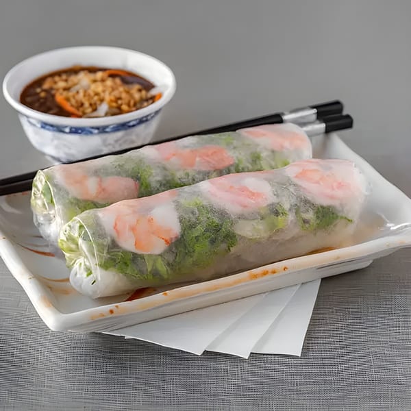 Two fresh Vietnamese spring rolls with shrimp and greens, chopsticks, and a dipping sauce.
