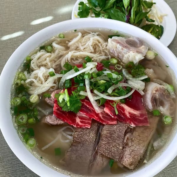 A bowl of Golden Deli pho with various cuts of beef, tripe, noodles, and fresh herbs.