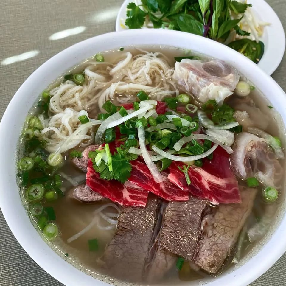 A bowl of Golden Deli pho with various cuts of beef, tripe, noodles, and fresh herbs.