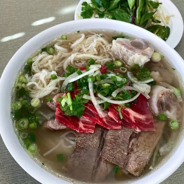 Golden Deli's pho with various cuts of beef, noodles, and fresh herbs in a white bowl.