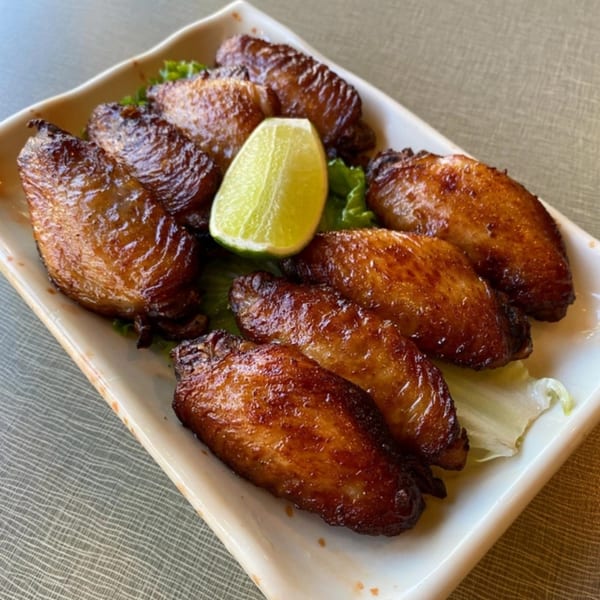 Golden Deli's Vietnamese chicken wings, glazed and golden brown, served with a lime wedge on lettuce.