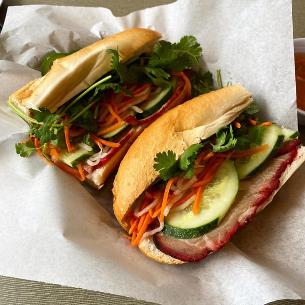 Two Golden Deli Vietnamese banh mi sandwiches with pork, cucumber, carrots, and cilantro on white paper.