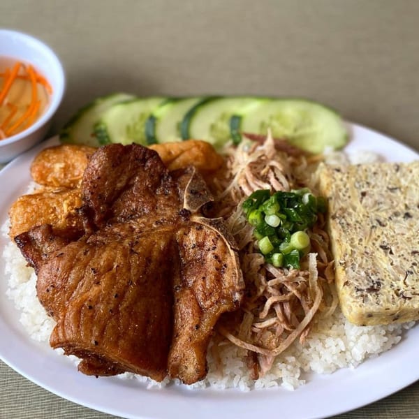 Vietnamese broken rice dish with grilled pork chop, shredded pork skin, egg cake, and cucumber slices.