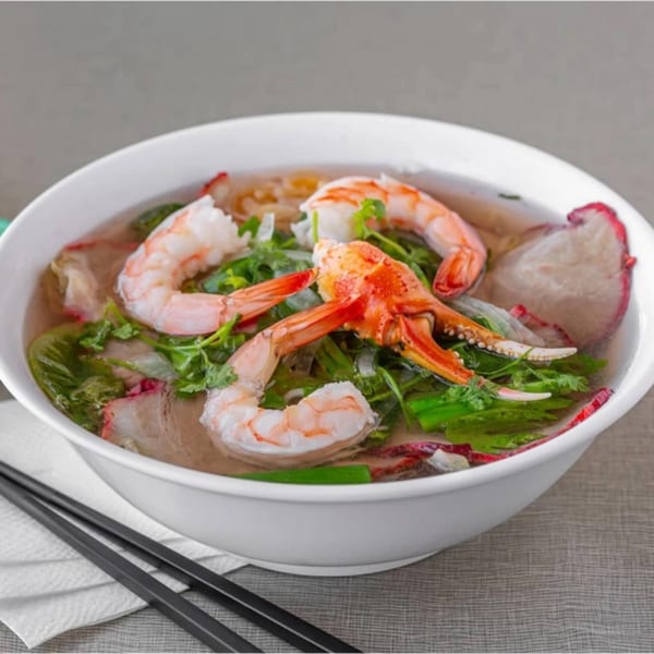 Golden Deli's Vietnamese noodle soup with shrimp, crab, and greens in a white bowl with chopsticks.