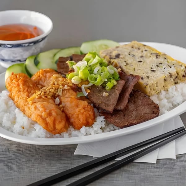 Vietnamese rice plate with fried shrimp, sliced beef, egg cake, cucumbers, and dipping sauce.